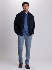 A man modeling a black utility jacket over a blue and white plaid button-down shirt, paired with light blue jeans and brown leather shoes, against a light gray studio background | Black