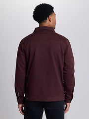 A man viewed from the back wearing a dark burgundy long-sleeve utility jacket and dark pants, standing against a light gray studio background. | Dark Oxblood
