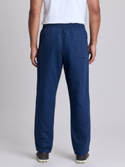 A man viewed from the back wearing navy blue relaxed-fit pants, a white t-shirt, and dark sneakers against a light gray studio background. | Deep Blue
