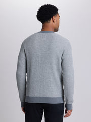 A man viewed from the back wearing a light gray textured knit sweater with darker gray ribbed trim at the collar, cuffs, and hem, paired with dark pants, against a light gray studio background.  | Dark Medium Grey Heather