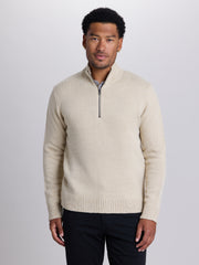 A man wearing a cream-colored textured knit quarter-zip sweater with a stand collar, paired with dark trousers, photographed against a neutral light gray studio background. | Chai