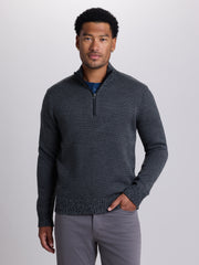 A man wearing a dark gray textured knit quarter-zip sweater over a blue undershirt and gray pants, standing against a light gray studio background. | Skillet