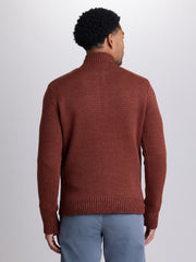 A man viewed from the back wearing a textured, ribbed-knit turtleneck sweater in a rust brown color, paired with light blue jeans, against a plain light gray studio background. | Redwood