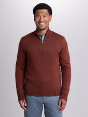 A man wearing a textured rust-brown half-zip sweater over a light blue collared shirt and gray pants, standing against a light gray studio background. | Redwood