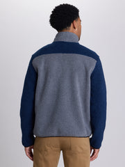 A man viewed from the back wearing a color-block fleece pullover with a gray body and navy sleeves, paired with tan pants, against a light gray studio background. | Charcoal