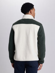 A man viewed from the back wearing a color-block fleece pullover with a cream sherpa back and dark green sleeves and shoulder yoke, paired with navy pants, against a light gray studio background. | Powder