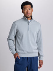 A man wearing a light gray quarter-zip pullover sweatshirt and navy blue pants, standing against a light gray studio background. | Cobra