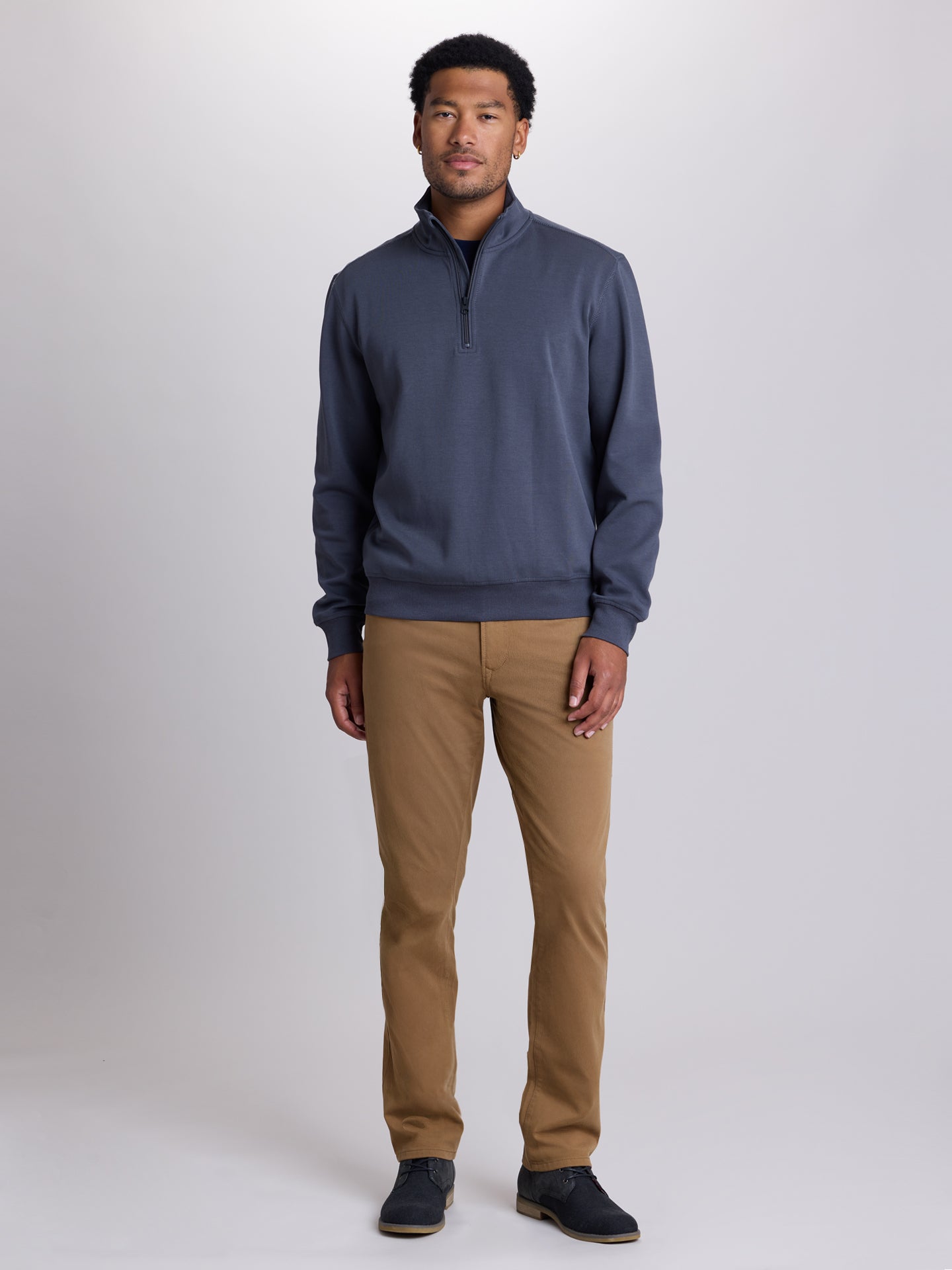 A man modeling a slate blue quarter-zip pullover sweater and tan chinos against a light gray studio background. | Chestnut