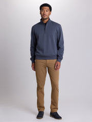 A man modeling a slate blue quarter-zip pullover sweater and tan chinos against a light gray studio background. | Chestnut