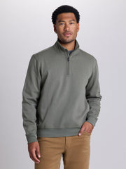A man wearing a sage green quarter-zip pullover sweater and tan pants, standing against a light gray studio background. | Cobra