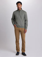 A man modeling a muted sage green quarter-zip pullover sweater paired with tan pants and dark blue shoes, standing against a light gray studio background. | Dusty Olive