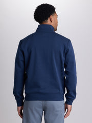 A man viewed from the back wearing a navy blue quarter-zip sweatshirt and light gray pants, set against a plain light gray studio background. | Starry
