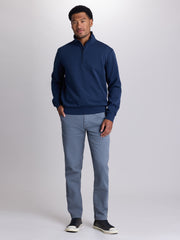 A man modeling a navy blue quarter-zip pullover sweater and light blue jeans against a light gray studio background. | Starry