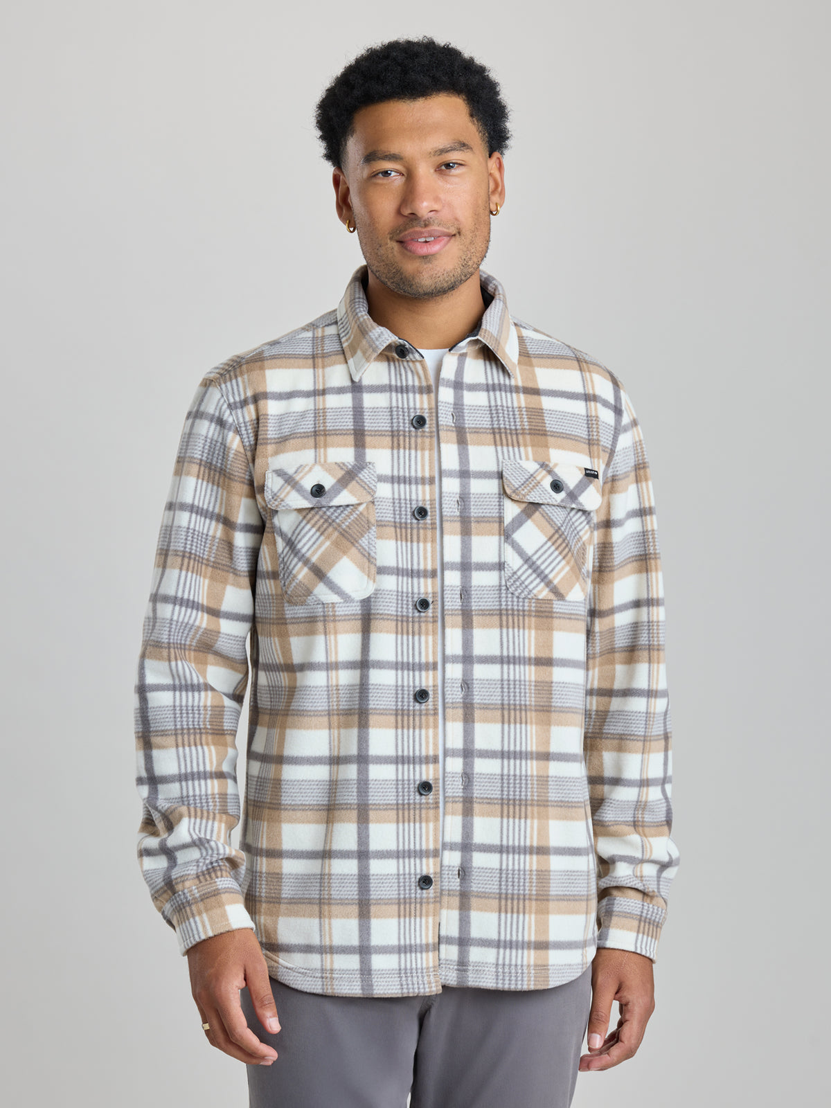 A man wearing a long-sleeve plaid button-up shirt in beige, brown, and gray tones, paired with gray pants, standing against a solid light gray studio background. | Steam