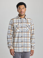 A man wearing a long-sleeve plaid button-up shirt in beige, brown, and gray tones, paired with gray pants, standing against a solid light gray studio background. | Steam