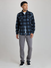 A man modeling a dark blue and black buffalo plaid flannel shirt over a white t-shirt, paired with gray pants and black sneakers, against a light gray studio background.  | Nightfall