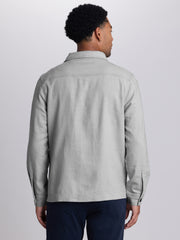 A man viewed from the back wearing a light gray linen-blend button-up shirt jacket and dark navy trousers, set against a plain light gray studio background. | Vapor