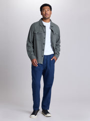 A man modeling a gray button-up overshirt over a white t-shirt, paired with navy blue pants and black sneakers, standing against a light gray studio background. | Deep Blue