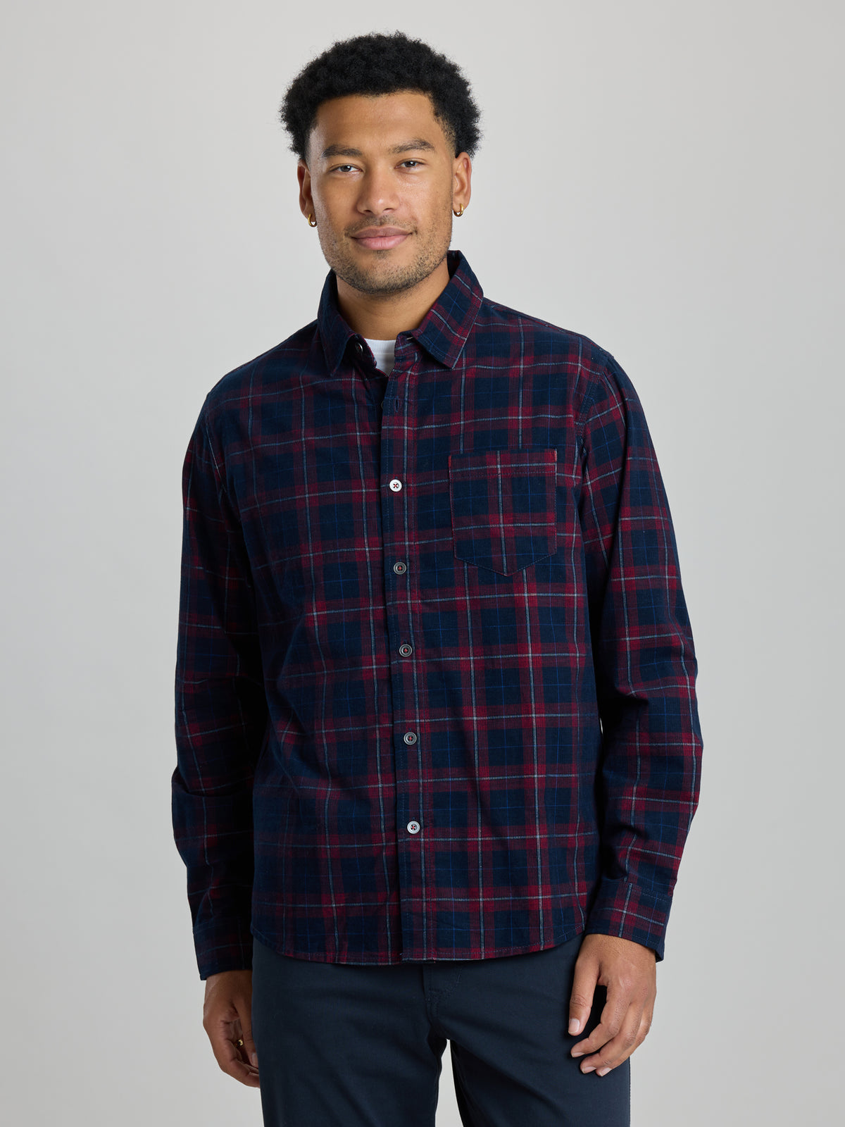 A man modeling a long-sleeve button-up plaid shirt in navy and red, paired with dark navy pants, against a light gray studio background. | Dark Night