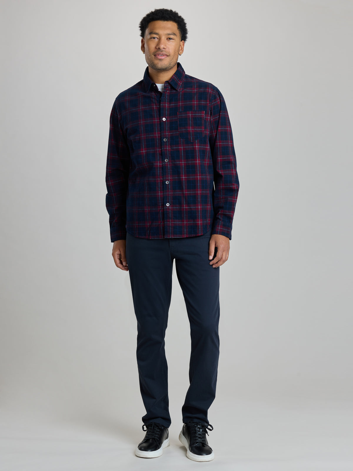 A man modeling a long-sleeve button-up plaid shirt in navy and red, paired with dark navy pants and black sneakers, against a light gray studio background. | Dark Night