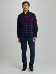A man modeling a long-sleeve button-up plaid shirt in navy and red, paired with dark navy pants and black sneakers, against a light gray studio background. | Dark Night