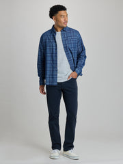 A man modeling a blue plaid button-down shirt over a light gray t-shirt, paired with dark navy pants and white sneakers, against a solid light gray studio background. | Blueprint