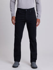 A person wearing slim-fit black jeans, a light gray long-sleeve shirt, and gray slip-on shoes, standing against a light gray studio background. | Black