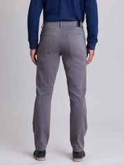 Rear view of a person wearing gray slim-fit trousers, a navy blue ribbed sweater, and dark shoes against a light gray studio background. | Grey Goose