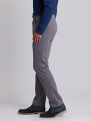 A side profile view of a person wearing slim-fit gray trousers, a navy blue long-sleeve top, and dark navy shoes against a light gray studio background. | Grey Goose