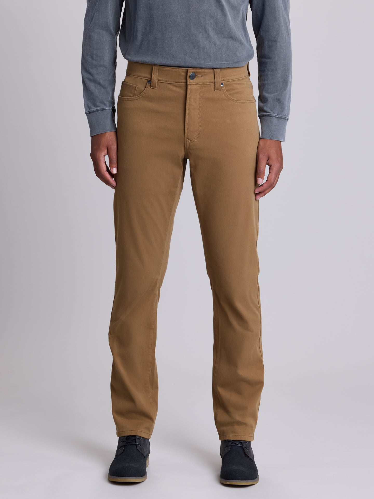 A person wearing slim-fit tan chinos with a blue long-sleeve shirt and dark navy shoes, shown from the waist down against a light gray studio background. | Chestnut