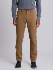 A person wearing slim-fit tan chinos with a blue long-sleeve shirt and dark navy shoes, shown from the waist down against a light gray studio background. | Chestnut