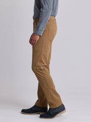 A side profile view of a person wearing tan chinos, a blue-gray long-sleeve shirt, and navy blue suede shoes against a light gray studio background. | Chestnut