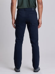 Rear view of a person wearing dark navy straight-leg trousers, a dark green shirt, and gray shoes against a light gray studio background. | Twilight