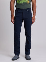 A man wearing dark navy blue straight-leg jeans, a green graphic t-shirt, and gray slip-on shoes, standing against a light gray studio background. | Twilight