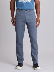 A person wearing slim-fit blue-gray chino pants, a blue graphic t-shirt, and black low-top sneakers, photographed against a light gray studio background. | Condor