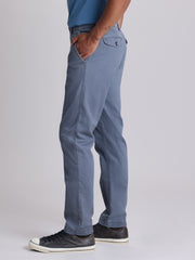 A person shown from the waist down wearing a pair of slim-fit blue chinos with black sneakers, standing against a light gray studio background. | Condor