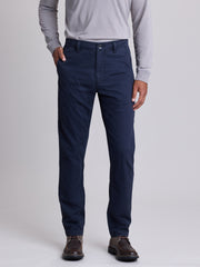 A person wearing navy blue straight-leg chino pants, a light gray long-sleeve shirt, and brown leather shoes, standing against a light gray studio background. | Twilight