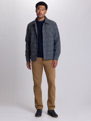 A man modeling a dark gray and blue plaid overshirt over a navy blue sweater, paired with tan pants and dark shoes, against a light gray studio background. | Forged