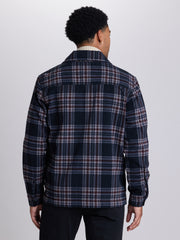 A man viewed from the back wearing a navy blue plaid overshirt with red and white stripes, paired with dark trousers, against a light gray studio background. | Deep Space