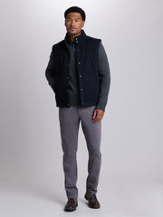 A man modeling a dark navy blue quilted vest with gray knit zip up, paired with gray trousers and brown shoes, against a light gray studio background. | Skillet